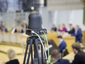 Eine Kamera ist im Plenarsaal auf das Geschehen gerichtet.