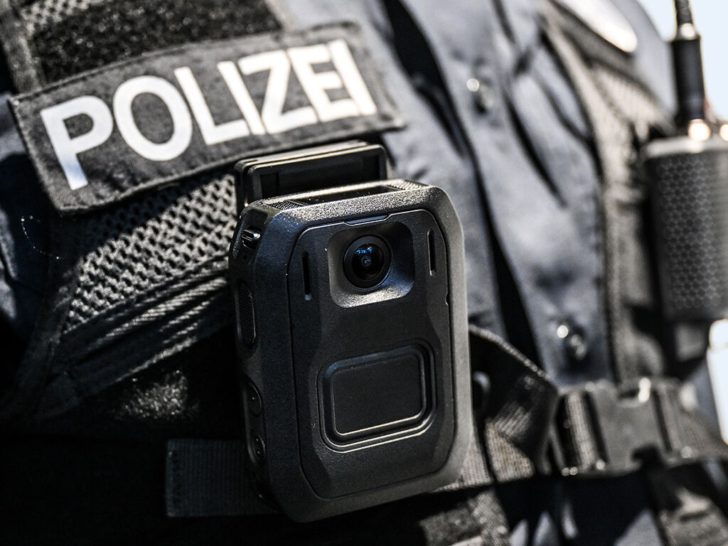 Ausschnitt einer schwarzen Polizeiuniform mit dem Schriftzug POLIZEI und einer Bodycam