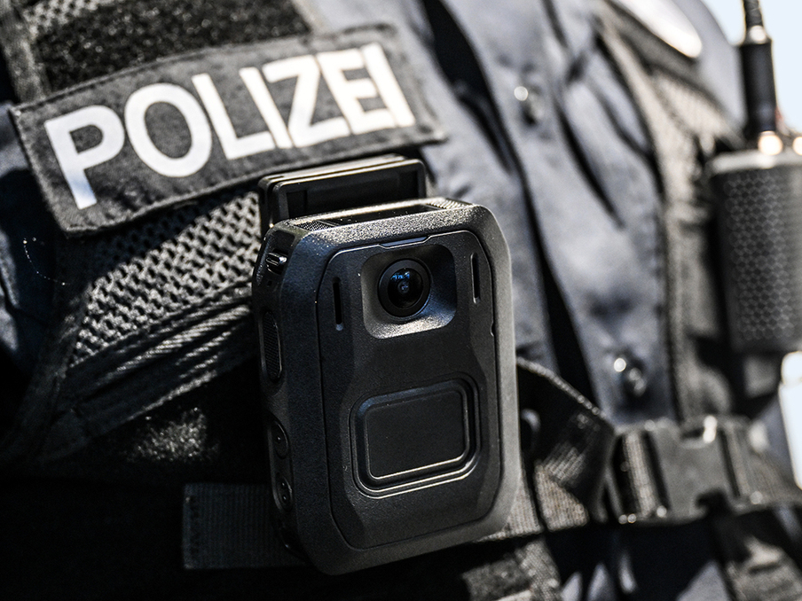 Ausschnitt einer schwarzen Polizeiuniform mit dem Schriftzug POLIZEI und einer Bodycam
