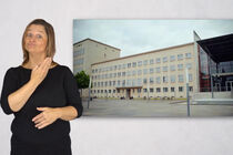 Eine Gebärdendolmetscherin zeigt mit Mimik und Gestik ein Wort oder einen Satz, neben ihr ist das Landtagsgebäude zu sehen