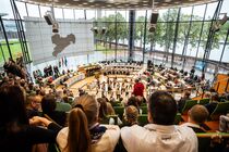 Auf der Besuchertribüne sitzen viele Menschen, die sich die Vorstellung der Tanzgruppe im Plenarsaal anschauen.
