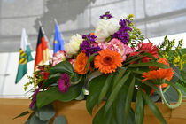 Bunter Blumenschmuck steht am Rednerpult , im Hintegrund sind Fahnen zu sehen.