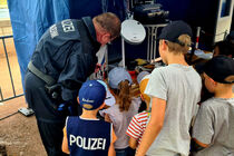 Mehrere Kinder stehen um einen Polizisten herum und schauen ihm zu.