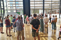 Eine Gruppe von Gästen steht in der Lobby und hört einer Besucherführerin zu.