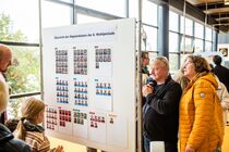 Menschen stehen vor ein großen Pinnwand, um sich die Listen der neuen Abgeordneten anzuschauen.
