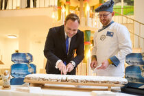 Landtagspräsident Alexander Dierks schneidet unter den Augen eines Bäckers en Stollen im Landtag an.